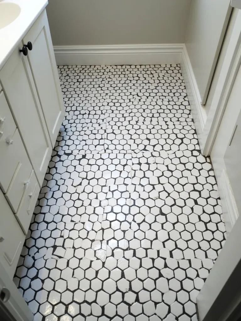 An overhead shot displaying a classic bathroom floor covered in black and white hexagon tiles, lit with soft, even light, that illustrates its integration into a broader bathroom context.