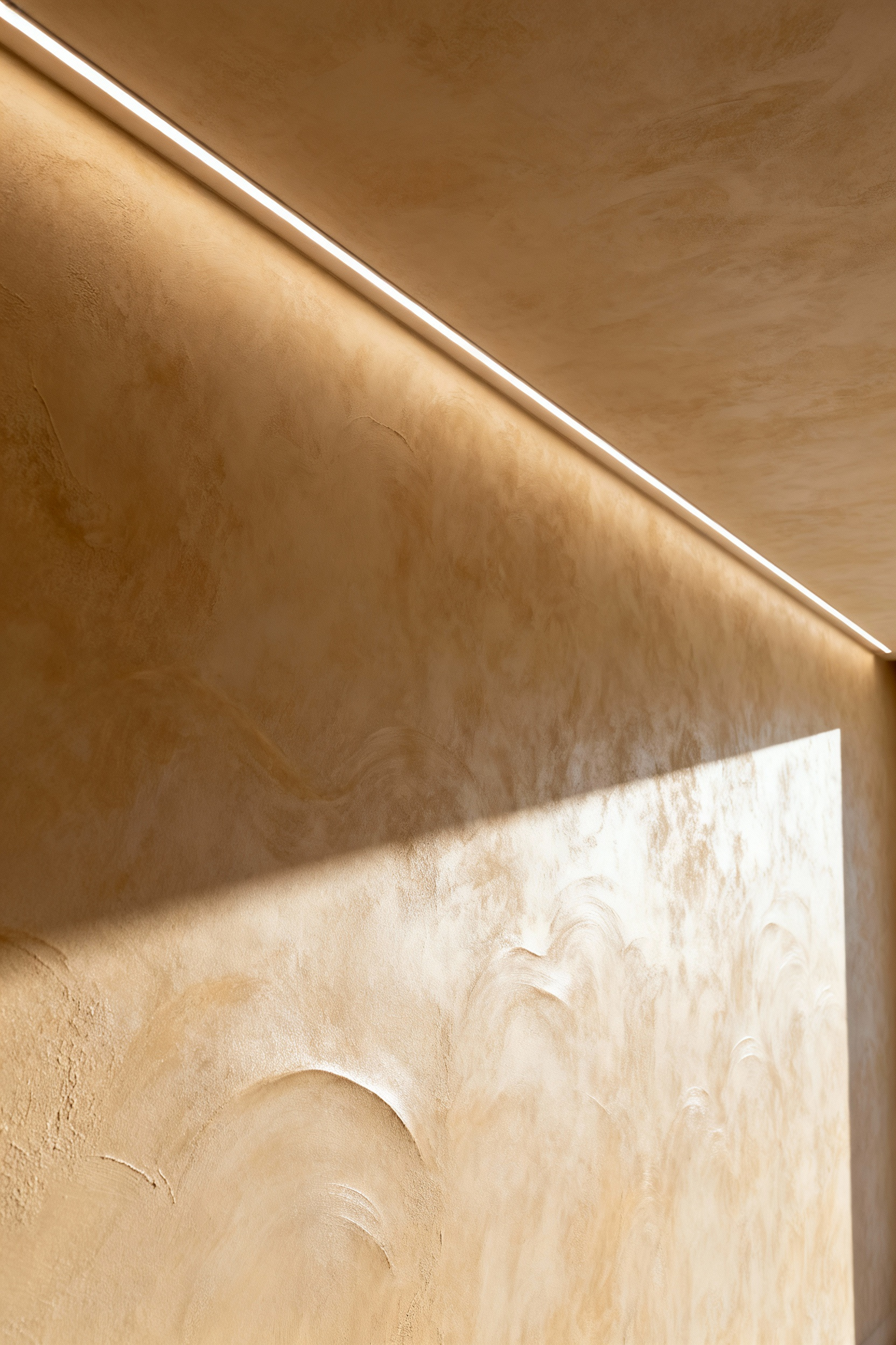 Luxurious living room wall featuring warm beige Venetian plaster with grazing integrated lighting highlighting its sophisticated texture and depth.